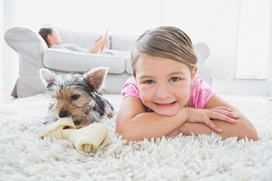Little girl lying on rug with yorkshire terrier smiling at camera at home in the living room