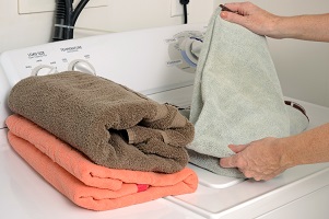 woman doing laundry and folding clean towels near washer and dryer